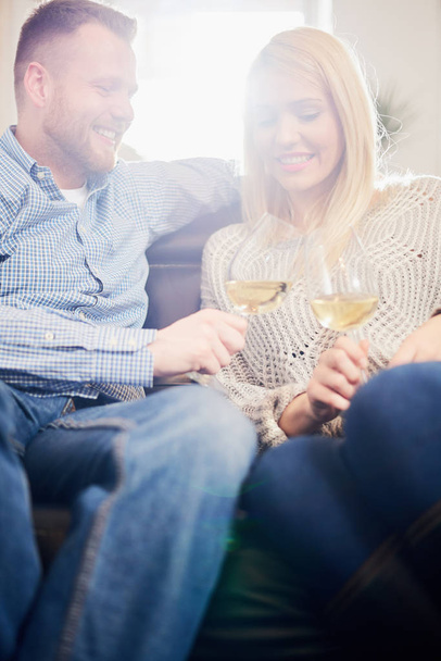 リビング ルームのソファに座ってワインを飲みながら白人のカップル  - 写真・画像