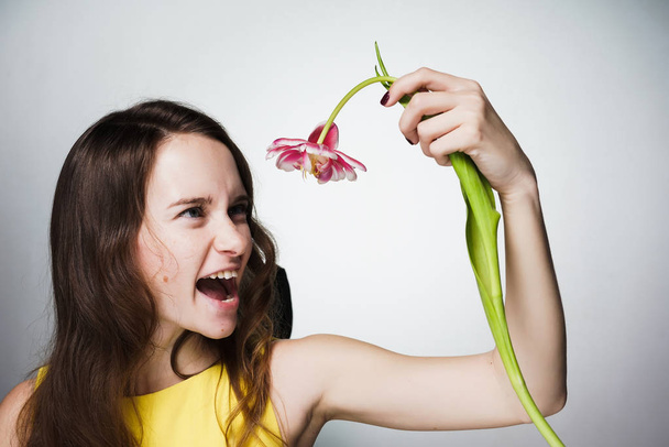 emotional beautiful girl dissatisfied with a gift for mother's day, holds a pink flower in her hands - Foto, Imagem