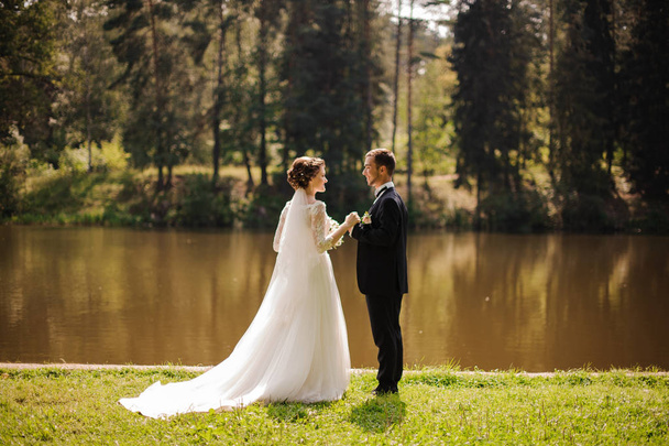 Young and beautiful bride with bridegroom on the river bank - Photo, Image