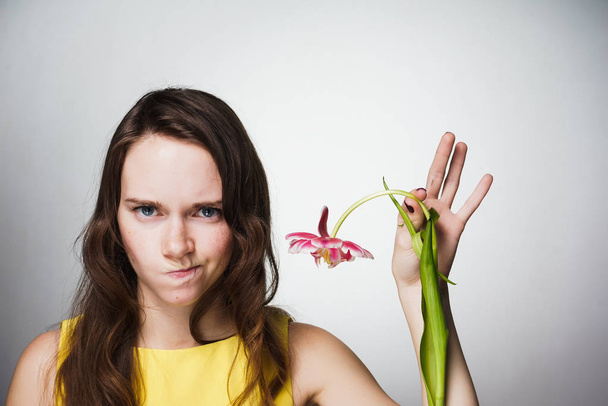 an angry young woman is unhappy with a gift on a world women's day, holds a flower in her hand - Фото, изображение