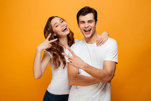 Cheerful young couple posing together while showing peace gestures - Foto, Imagem