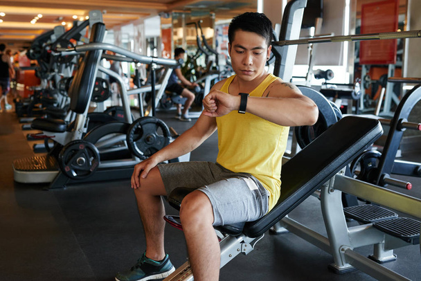 Hombre vietnamita comprobando sus resultados en reloj inteligente después de entrenar en el gimnasio
 - Foto, Imagen