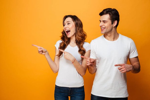 Portrait of a cheerful young couple pointing fingers away - Foto, imagen