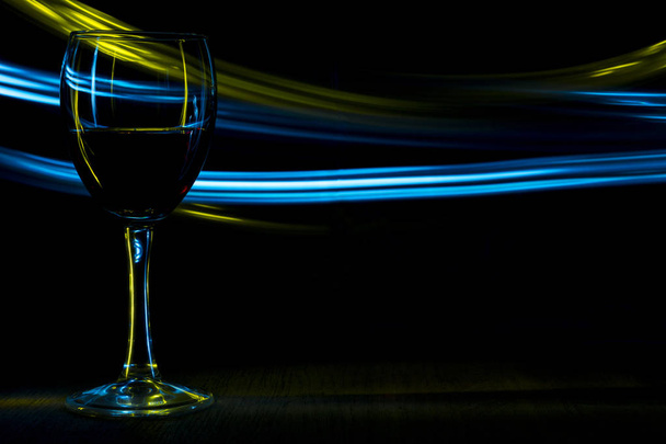 A glass of red wine in night club. Yellow and blue blurred bands. - Photo, image