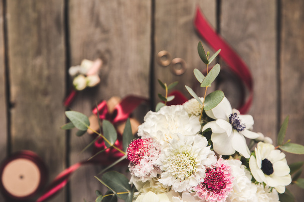 selective focus of beautiful bridal bouquet, wedding rings and ribbons on wooden surface - Foto, Bild