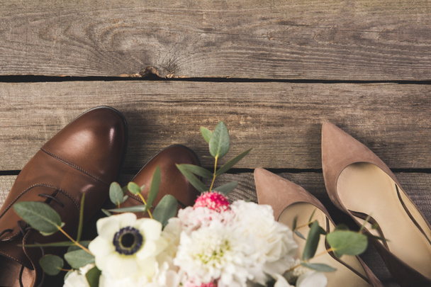 Draufsicht von Braut- und Bräutigamsschuhen mit Blumenstrauß auf Holztischplatte - Foto, Bild