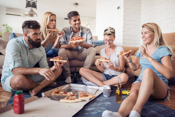 Gruppe spielfreudiger junger Leute isst Pizza und amüsiert sich gleichzeitig. - Foto, Bild