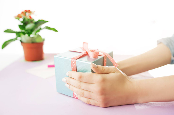 Close-up of female hands holding a present. The trendy pink desk. - 写真・画像