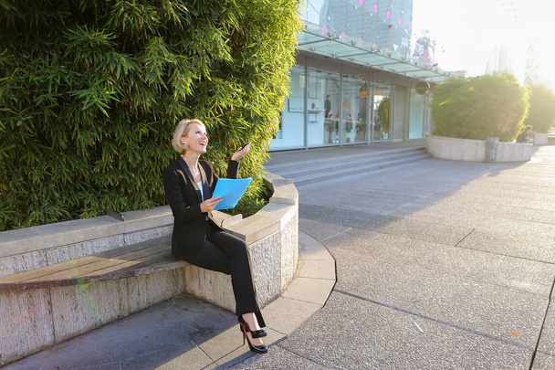 Sekretärin spricht im Freien per Smartphone mit Aktenkoffer - Foto, Bild