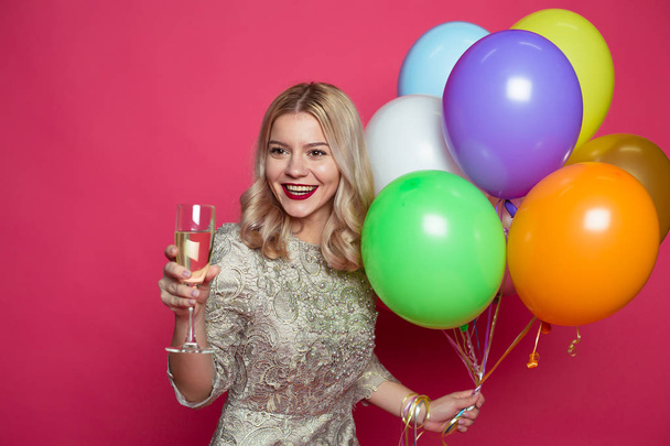 Elegante joven sonriente hermosa mujer rubia en vestido de noche sobre un fondo rosa con grandes bolas de helio multicolor. Fiesta de cumpleaños. Concepto de regalos y felicitaciones
. - Foto, imagen