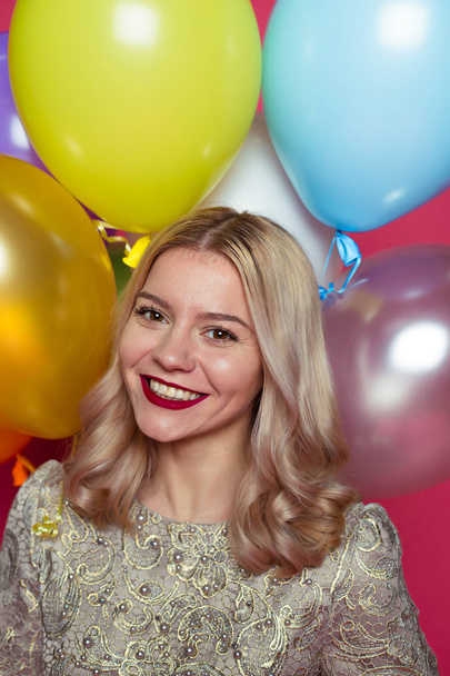 Birthday party. Concept of gifts and congratulations. Stylish young smiling beautiful blonde woman in evening dress on a pink background with large multi-colored helium balls. - Photo, Image