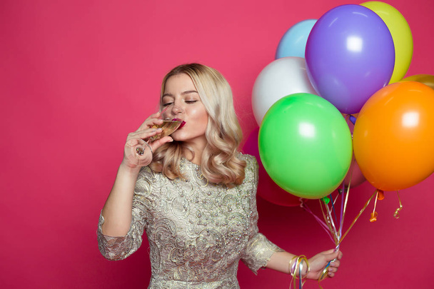 Stylish young smiling beautiful blonde woman in evening dress on a pink background with large multi-colored helium balls. Birthday party. Concept of gifts and congratulations. - Foto, imagen