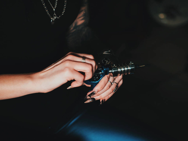 Artist prepares tools and machine for tattoo session, woman holding a tattoo gun. The tattooist checks the machine for performance, puts a needle inside the tube grip - 写真・画像