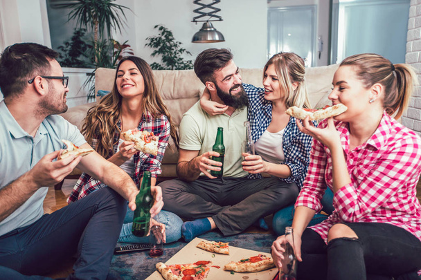 Grupo de jovens amigos comendo pizza na festa em casa
. - Foto, Imagem