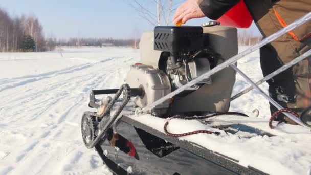 Man giet brandstof in de gastank van een mini sneeuwscooter op een winter besneeuwde weg - Video
