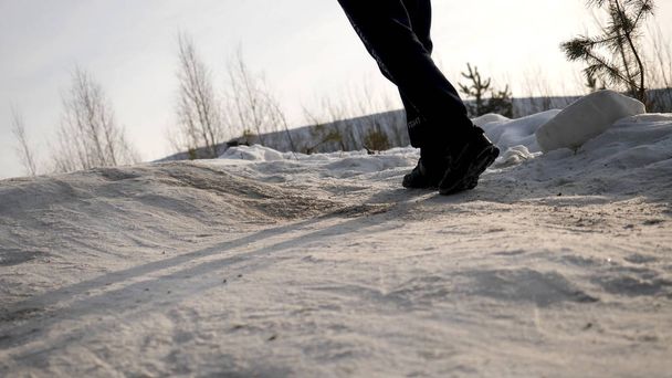 Close-up of male legs in winter shoes walking on snow. View of walking on snow with Snow shoes and Shoe spikes in winter. Mens legs in boots close up the snow-covered path - Photo, Image
