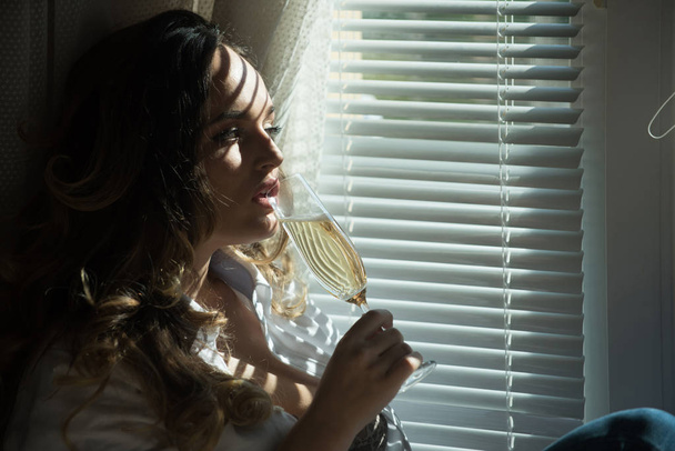 Girl with long curly hair drink champagne at window - Φωτογραφία, εικόνα