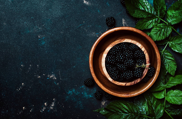 Fresh blackberries with green leaves in a bowl, food background, top view - Photo, Image