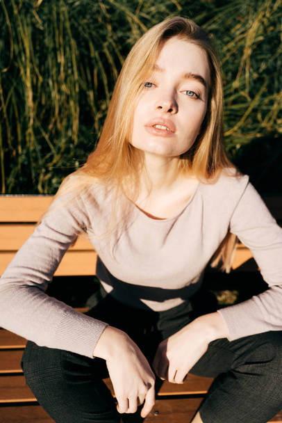 beautiful blue-eyed girl blonde is sitting on a bench outdoors. enjoys the sun - Fotó, kép
