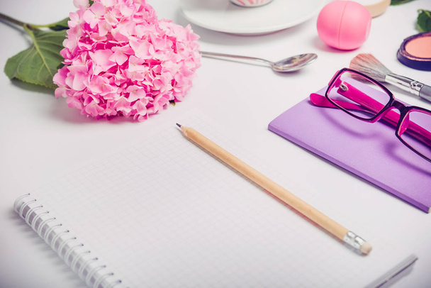 Top view Female working place with notebook for planning, cosmetic, sketchbook, glasses, and wisteria flowers on the white background. Fashion, Beauty blog concept. - Fotó, kép
