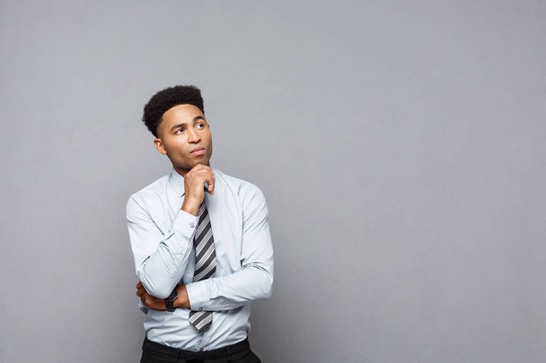 Бизнес - уверенный молодой афроамериканец, держащий руку на подбородке и думающий о бизнесе
. - Фото, изображение