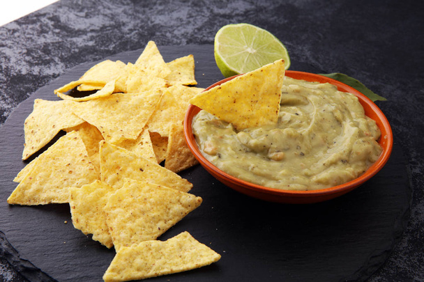 Bowl of guacamole with tortilla chips on dark background - Фото, зображення