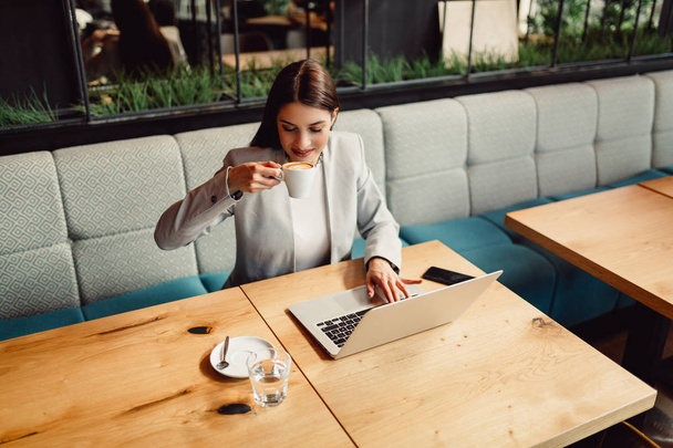 Beautiful businesswoman enjoying a coffee in front of her laptop computer - Zdjęcie, obraz