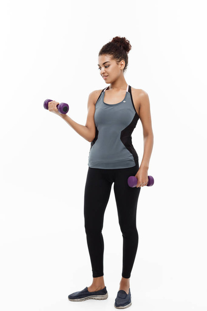 Healthy and Fitness concept - Full-length of portrait Beautiful American African lady in grey fitness clothes workout with dumbbell. Isolated on white background. - 写真・画像