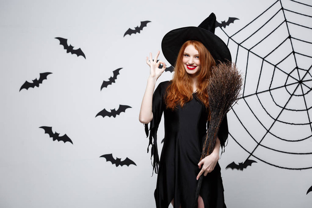 Conceito de Halloween - Bruxa elegante feliz gosta de brincar com vassoura festa de Halloween sobre fundo cinza
.  - Foto, Imagem