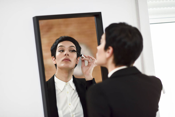 Young woman with very short haircut, putting makeup on in front  - Photo, Image