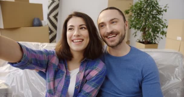 junges glückliches kaukasisches Paar, das an einem einziehenden Tag schöne und lustige Selfies auf der Couch zwischen Kisten und Sachen macht. Neue Heimat. Nahaufnahme. Innenräume - Filmmaterial, Video