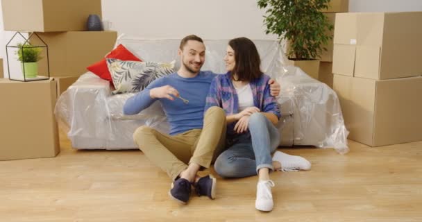 ボックスとかに囲まれて座っている間彼らの新しいアパートからキーを保持することによって幸福と楽しいうれしそうな若いカップル。中に - 映像、動画