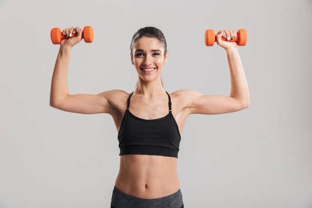 Image of happy strong woman putting small dumbbells up in air is - Zdjęcie, obraz