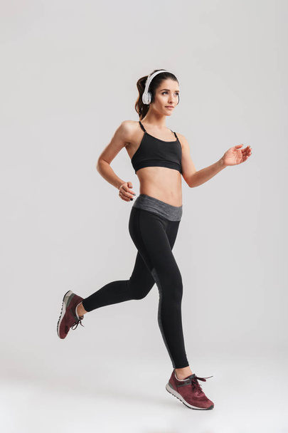 Full-length image of sporty woman in tracksuit running and liste - Foto, imagen