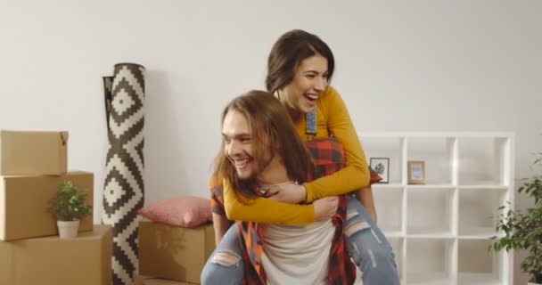 Portrait shot of young Caucasian just married couple having fun and being happy in their new apartment among home stuff during moving in it. Indoors - Footage, Video