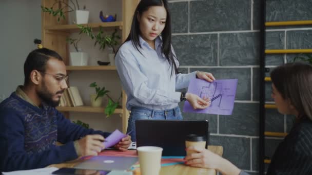 Young asian woman presenting paper architectural plan of house to multi ethnic team in modern start-up office - Séquence, vidéo