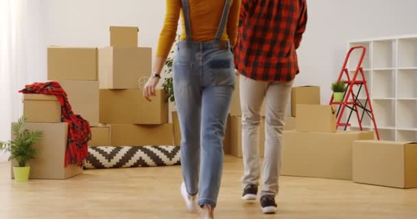 Back view of the young attractive couple stepping in the new cozy apartment on the moving in day, smiling and turning to the camera among unpacked boxes and home stuff in the living room. Inside - Footage, Video