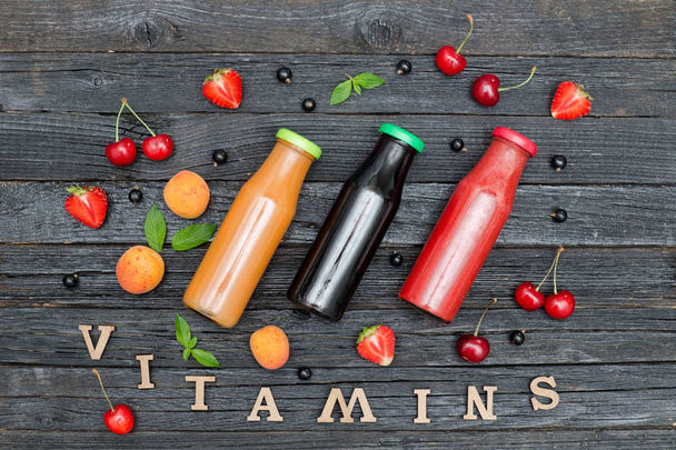 Três garrafas de suco, fruta e inscrição Vitaminas. Fundo de madeira
 - Foto, Imagem