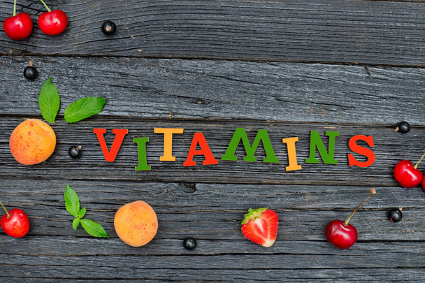 Väri kirjoitus Vitamiinit ja hedelmät. Musta puinen tausta
.  - Valokuva, kuva