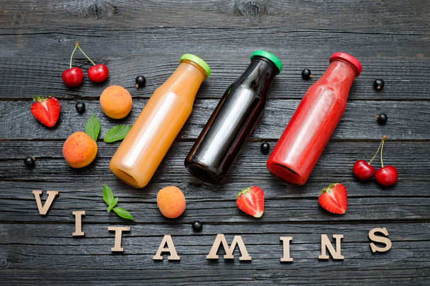 Tre bottiglie di succo, frutta e iscrizione Vitamine. Sfondo in legno
 - Foto, immagini