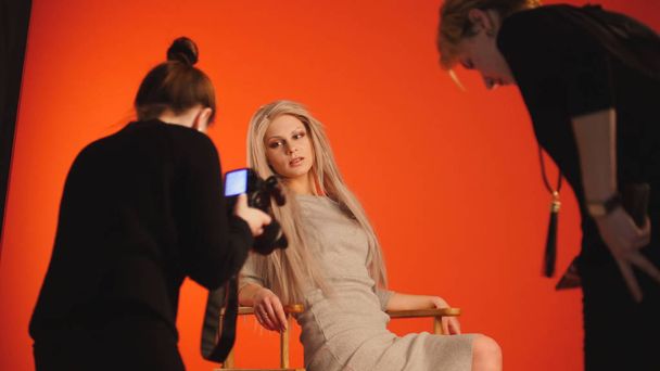 Menina modelo loira deitada no estúdio de fotos fotógrafo e maquiador endireita o cabelo, moda nos bastidores
 - Foto, Imagem