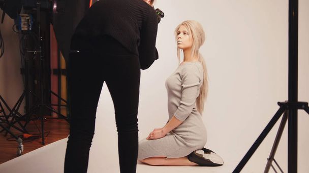 Warsztaty z za kulisami - blond dziewczyna piękny pozowanie dla fotografa - model siedzi na kolanach - Zdjęcie, obraz