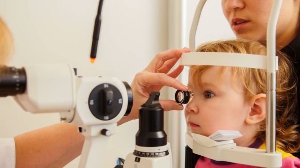 Childs healthcare - little girl with her mother in ophthalmological clinic checks eyesight vision - Photo, Image