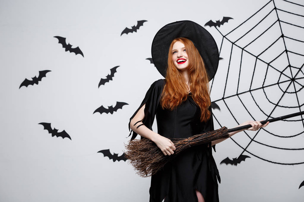 Conceito de Halloween - Bruxa elegante feliz gosta de brincar com vassoura festa de Halloween sobre fundo cinza
.  - Foto, Imagem