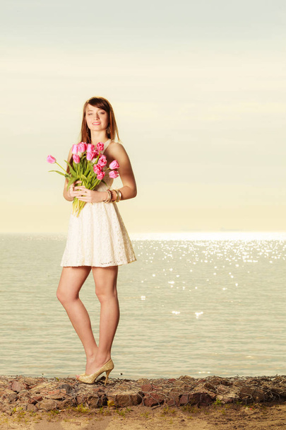 Beautiful woman holding bouquet of flowers on beach - Fotó, kép