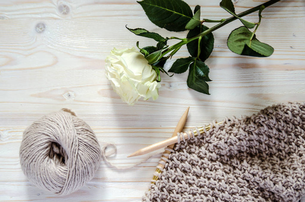 Een hoorn van merino wol garens, brei op breinaalden en een witte roos op een houten ondergrond. - Foto, afbeelding