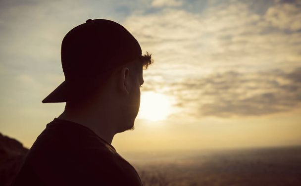 Silhouette eines jungen Mannes, der allein vor dem Sonnenuntergang steht - Foto, Bild