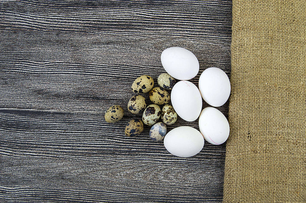 Белые куриные яйца и перепелиные яйца стоят бок о бок на деревянном полу
 - Фото, изображение