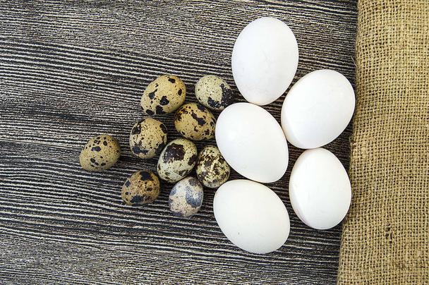 Jaja białe kurczaka i jaj przepiórczych stoją obok siebie na drewnianą podłogę - Zdjęcie, obraz