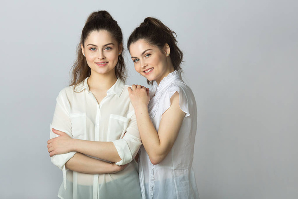 two beautiful smiling girl sisters twins in white blouses on a light background - Valokuva, kuva